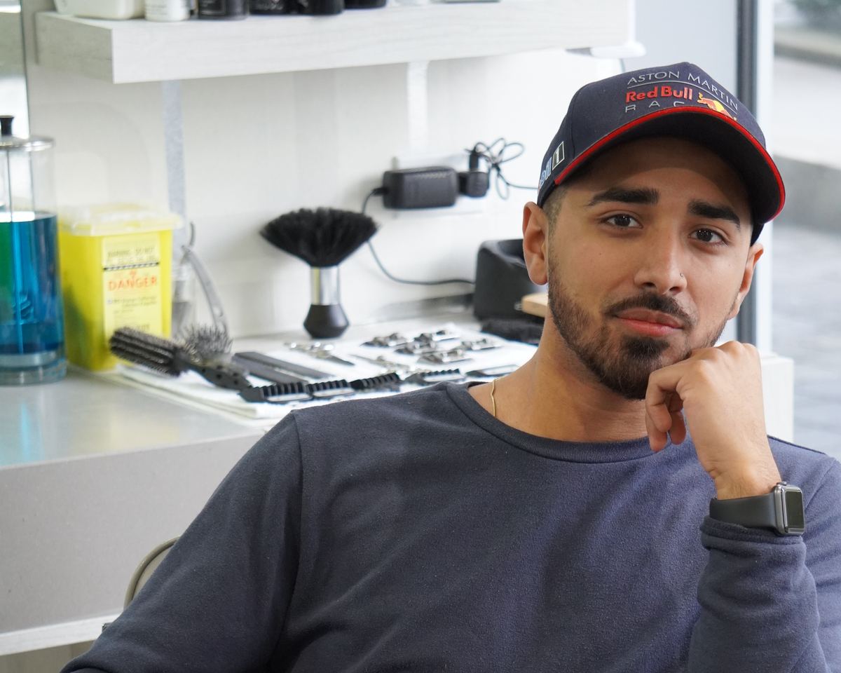 A barber seated at his station, his tools laid out on the counter behind him.