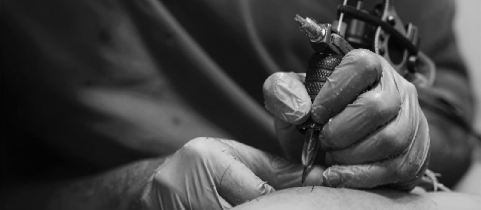A tattoo artist's gloved hands working a machine over fresh line work.